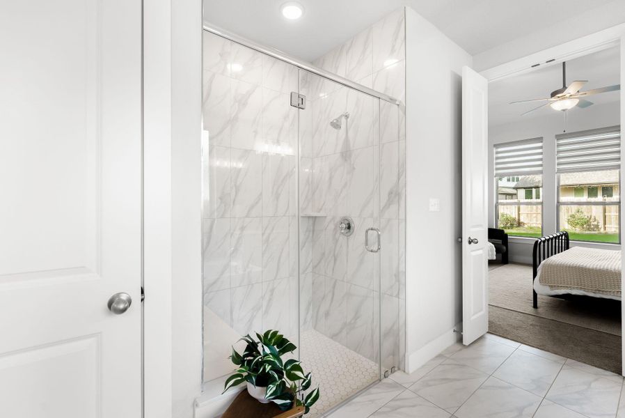 A modern glass-enclosed shower boasts white marble-look tile walls and hexagon floor tiles.