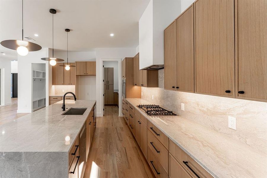 Kitchen with sink, light stone counters, decorative light fixtures, appliances with stainless steel finishes, and light wood-type flooring