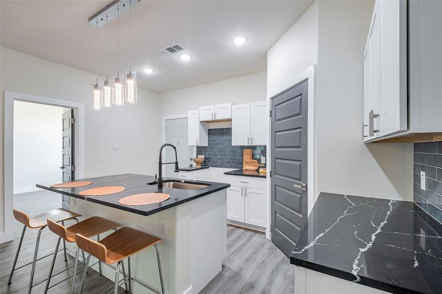 Kitchen with decorative backsplash, sink, light wood-type flooring, pendant lighting, and white cabinets