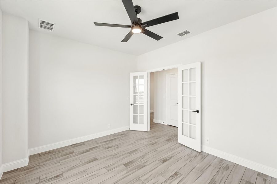 Empty room with light wood floors, black ceiling fan, and white French doors