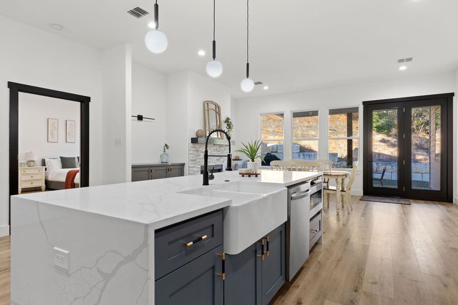 Kitchen with light stone counters, pendant lighting, a kitchen island with sink, light wood finished floors, and appliances with stainless steel finishes