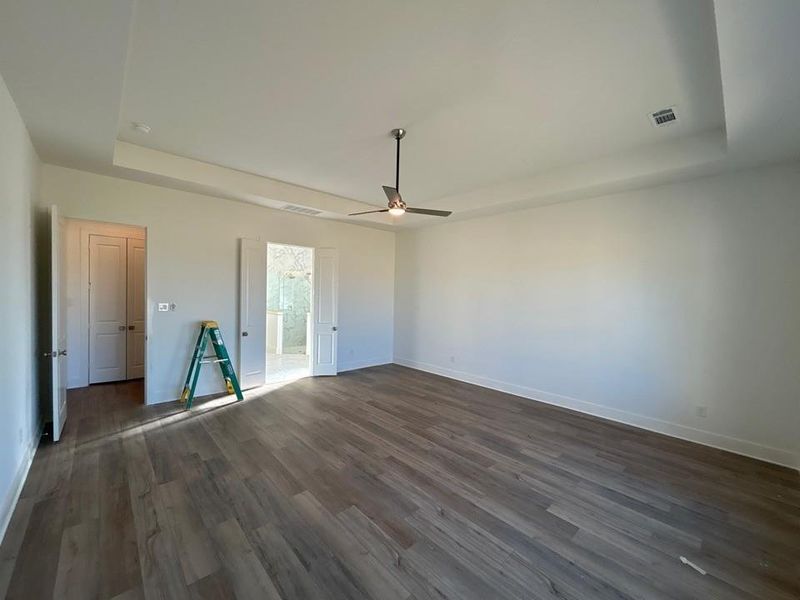 Unfurnished bedroom with a tray ceiling, ceiling fan, dark wood-type flooring, and ensuite bathroom
