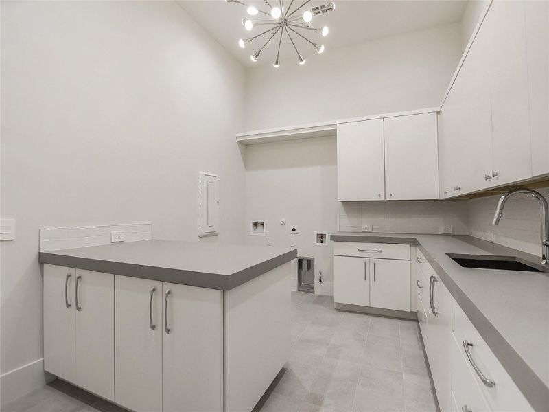 Spacious utility room featuring white cabinetry, grey countertops, a sink with a chrome faucet, and tile flooring