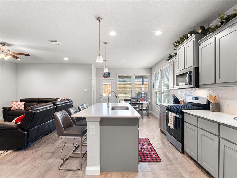 Kitchen featuring appliances with stainless steel finishes, a kitchen island with sink, gray cabinetry, and sink