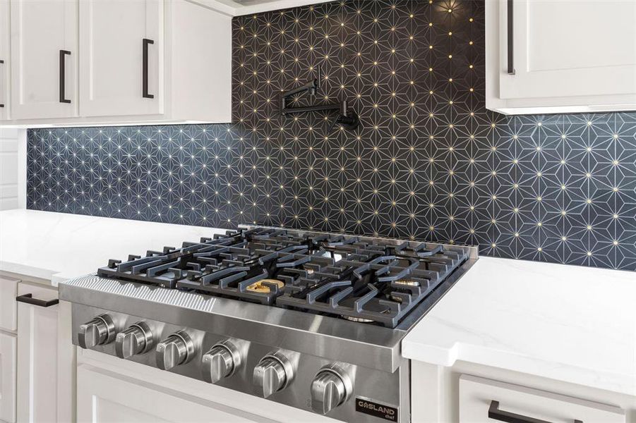 Room details featuring decorative backsplash, cooktop, and white cabinets