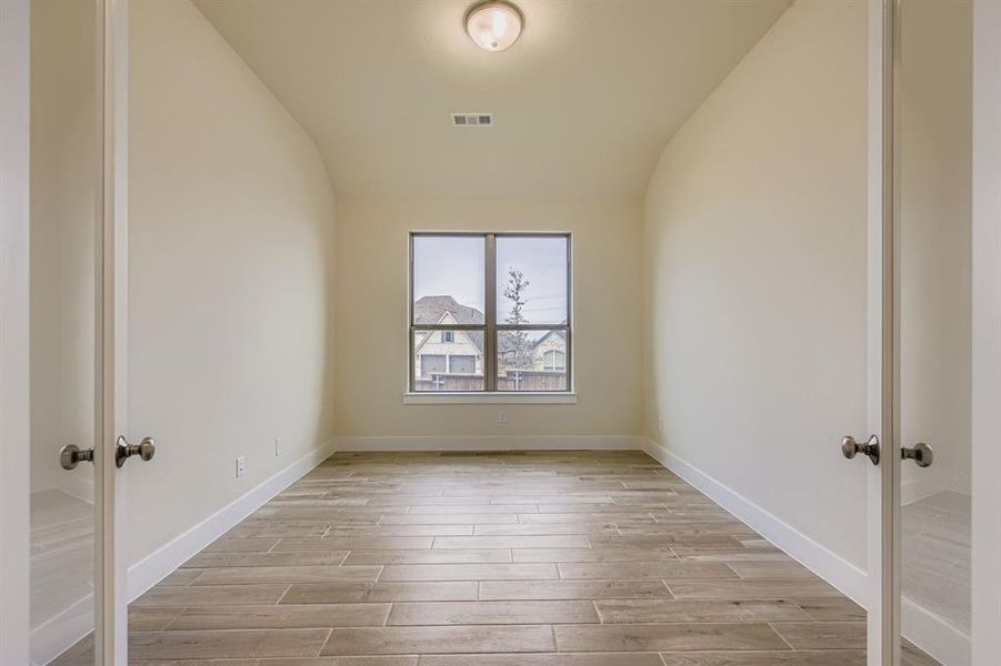 Empty room featuring wood tiled floors, french doors, and vaulted ceiling
