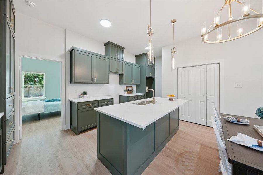 Kitchen featuring light wood-type flooring, a chandelier, decorative light fixtures, green cabinets, and an island with sink Kitchen featuring light wood-type flooring, a chandelier, decorative light fixtures, green cabinets, and an island with sink