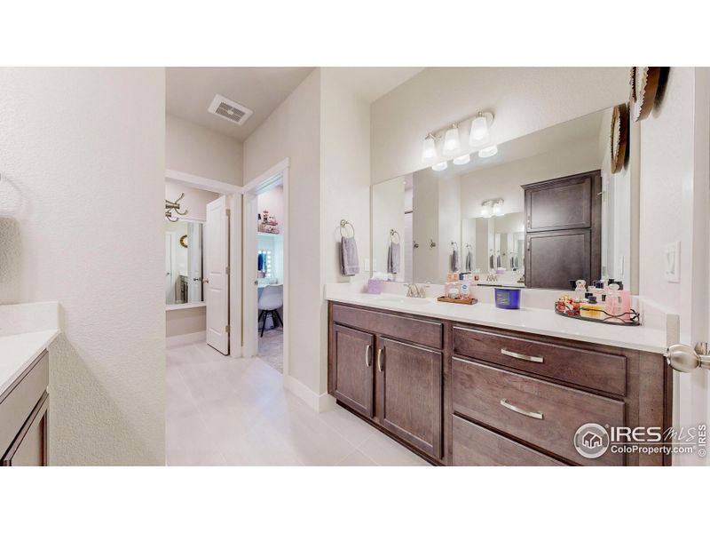 Primary suite bathroom has dual vanities on separate sides of bathroom (peak at the custom built vanity inside the walk-in closet)