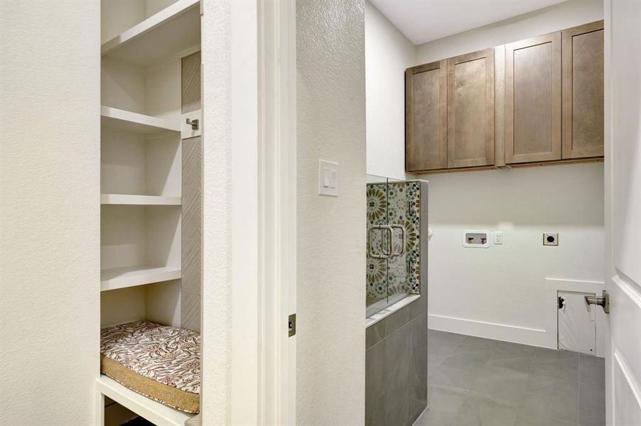Utility space featuring overhead cabinetry, patterned tile, and a built-in dog wash stall with glass doors Utility space featuring overhead cabinetry, patterned tile, and a built-in dog wash stall with glass doors