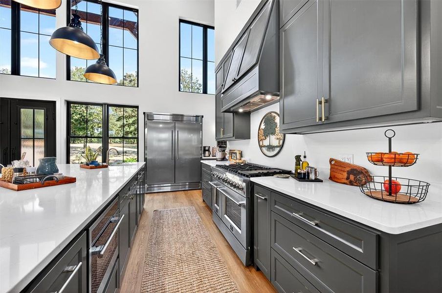 Kitchen featuring high end appliances, light stone countertops, light wood finished floors, premium range hood, and pendant lighting Kitchen featuring high end appliances, light stone countertops, light wood finished floors, premium range hood, and pendant lighting