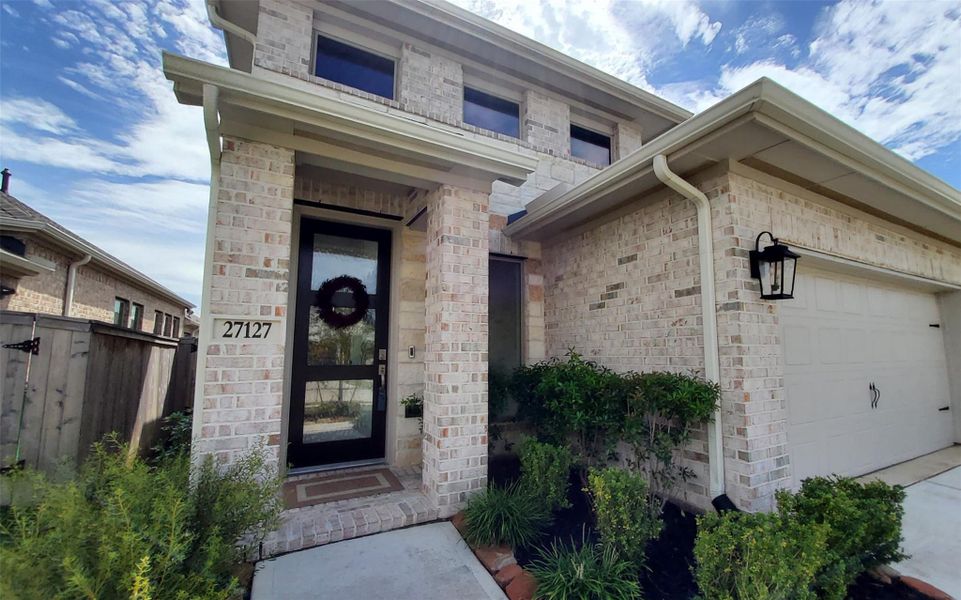 Charming brick home with a welcoming covered entry, modern black door, and neatly landscaped front yard.