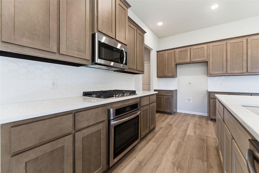 Kitchen with stainless steel appliances, light wood finished floors, decorative backsplash, recessed lighting, and light stone countertops