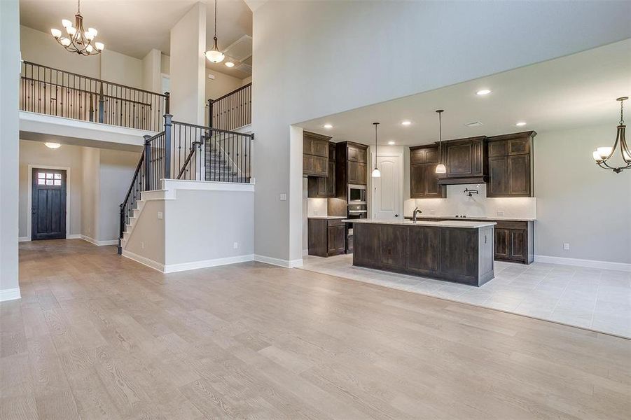 Kitchen with a high ceiling, a kitchen island with sink, hanging light fixtures, dark brown cabinets, and light wood-type flooring