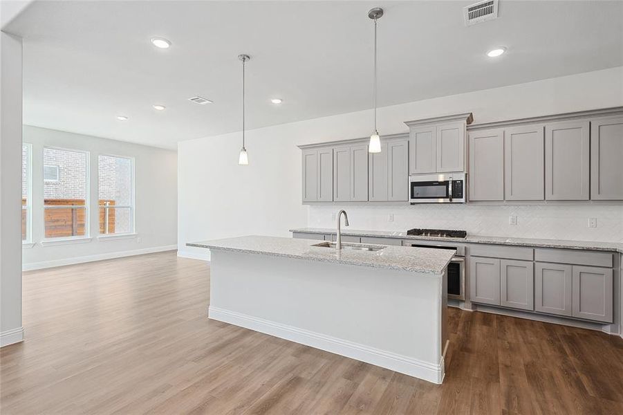 Kitchen featuring gray cabinetry, light stone counters, hanging light fixtures, and stainless steel appliances Kitchen featuring gray cabinetry, light stone counters, hanging light fixtures, and stainless steel appliances