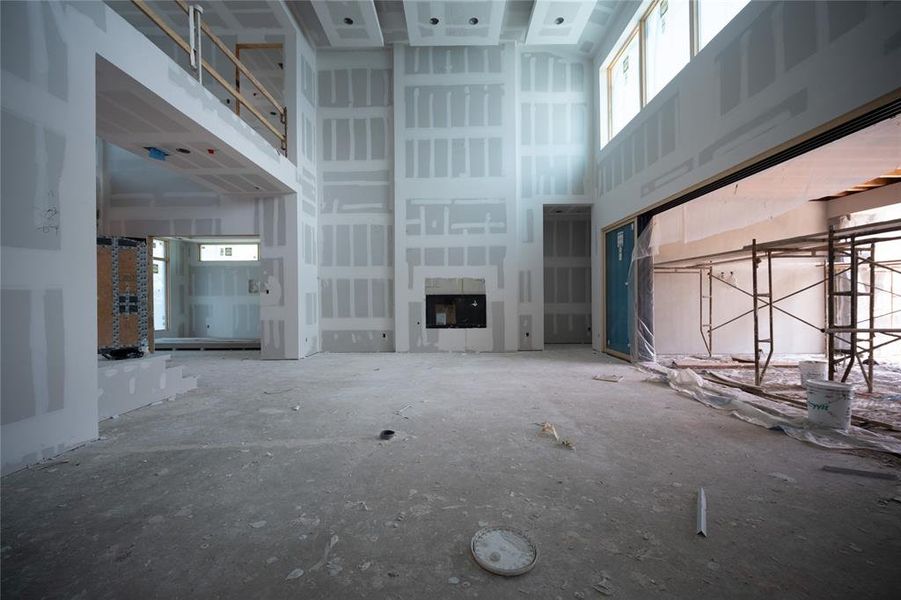 View from kitchen. Soaring ceiling with open floor plan. View of fire place, feature wall, office, primary suite, and glass sliders to patio/pool.