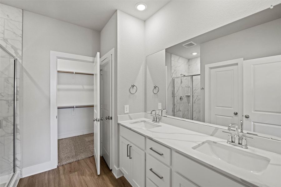 Spa-inspired ensuite with dual vanities, a soaking tub, separate glass-enclosed shower, and a large walk-in closet.