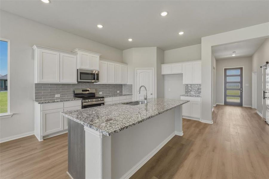Kitchen featuring a large central island with granite countertop, white cabinetry, stainless steel appliances, and a gray subway tile backsplash Kitchen featuring a large central island with granite countertop, white cabinetry, stainless steel appliances, and a gray subway tile backsplash