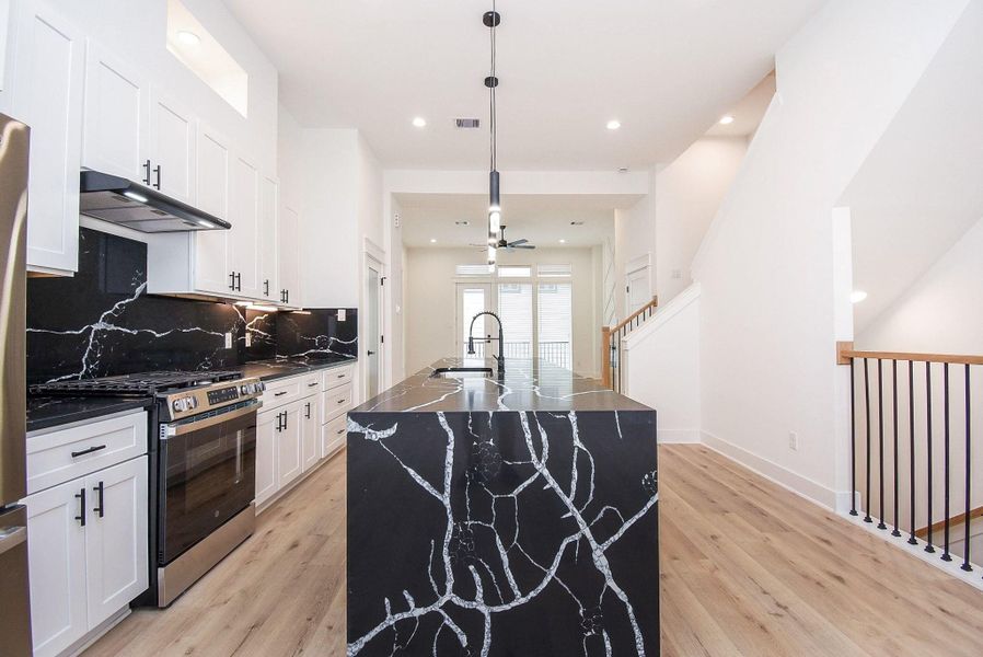 This modern kitchen features sleek white cabinetry, a striking black marble island with unique veining, and stainless steel appliances. The open layout is complemented by light wood flooring and ample natural light, creating an inviting and stylish space.