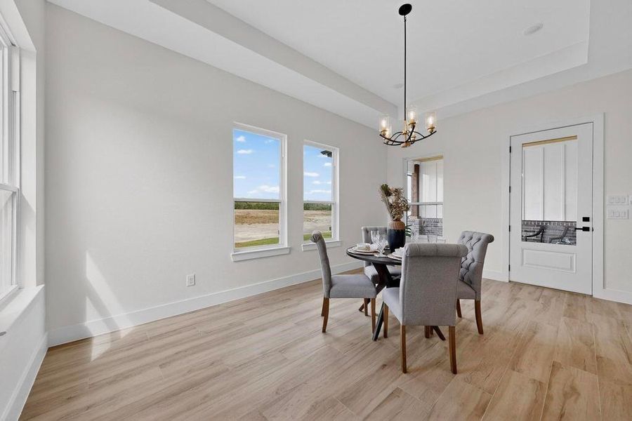 Dining area with light wood-type flooring, a tray ceiling, and a chandelier Dining area with light wood-type flooring, a tray ceiling, and a chandelier