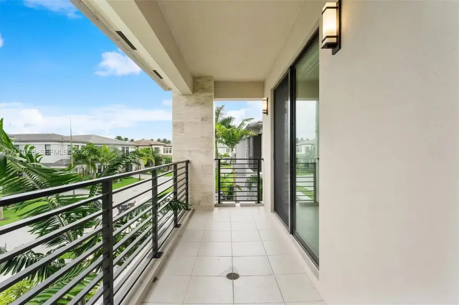 Covered balcony featuring large-format tile flooring, stone-clad pillar, metal horizontal railing, and wall-mounted exterior light fixtures