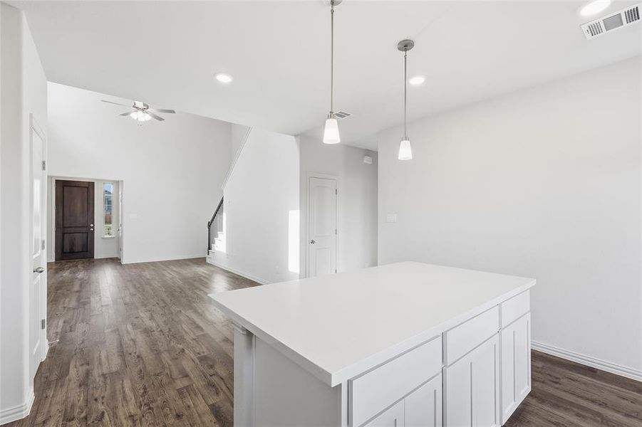 Open-concept living space featuring wood-finish flooring, a contemporary kitchen island with pendant lighting, and a vaulted ceiling