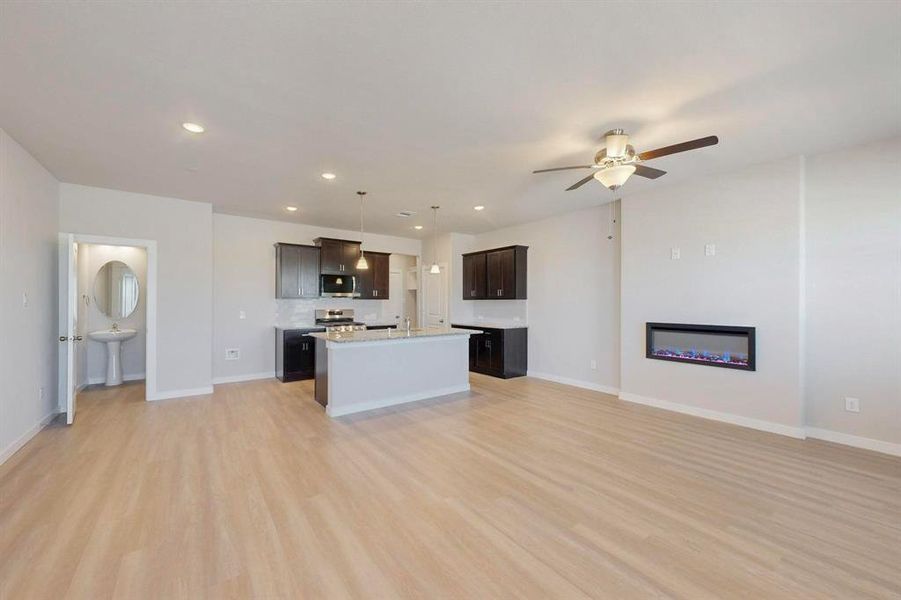 Kitchen with open floor plan, dark brown cabinets, light wood-type flooring, recessed lighting, and a fireplace