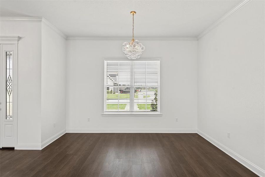 Empty room with a chandelier, dark wood finished floors, and crown molding Empty room with a chandelier, dark wood finished floors, and crown molding