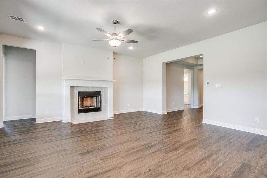 Unfurnished living room featuring ceiling fan, a tiled fireplace, and dark wood-type flooring