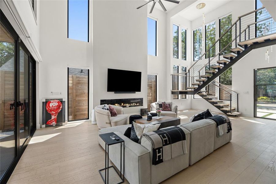 Living room with fireplace, grand stairway, light wood flooring, and custom electric shades