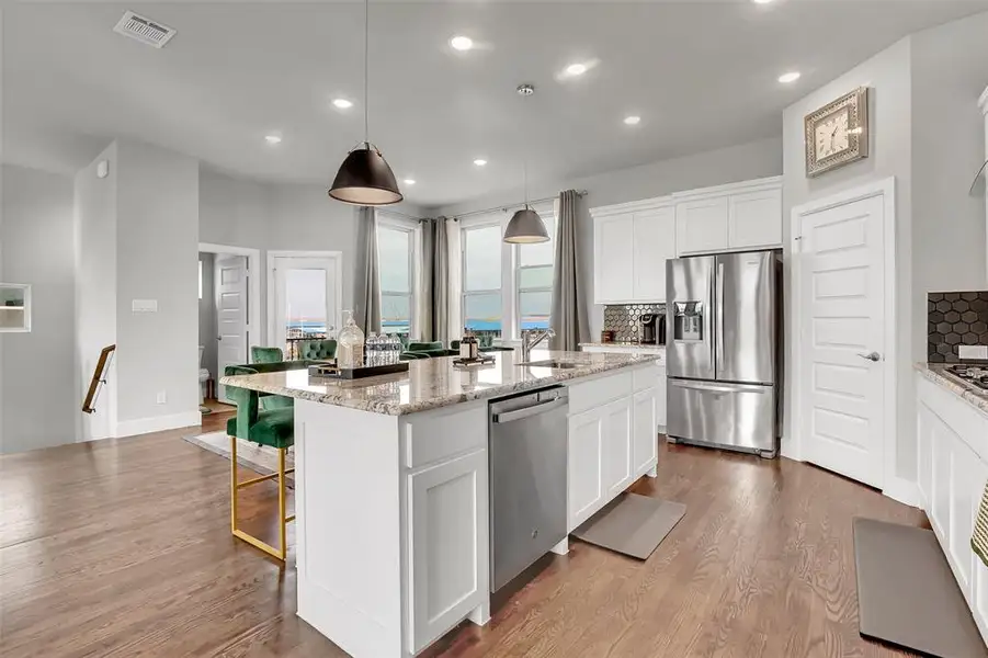 Kitchen featuring stainless steel appliances, white cabinets, tasteful backsplash, light stone counters, and a kitchen island with sink