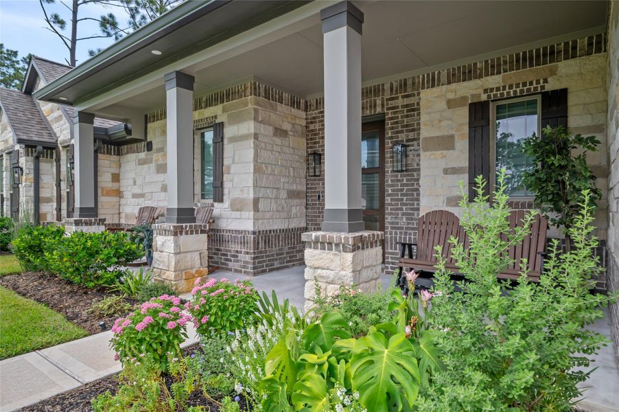 Oversized covered front porch with stone-and-brick accents and lush landscaping.