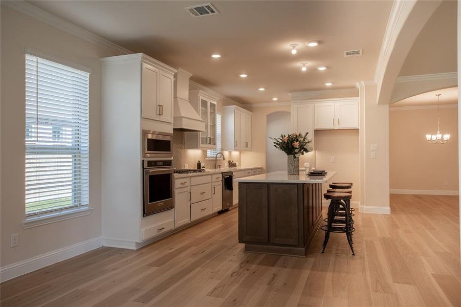 Kitchen featuring light hardwood / wood-style flooring, custom range hood, a center island, white cabinetry, and appliances with stainless steel finishes