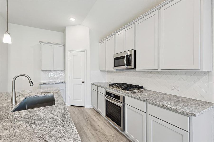 Kitchen featuring appliances with stainless steel finishes, tasteful backsplash, light hardwood / wood-style flooring, sink, and pendant lighting