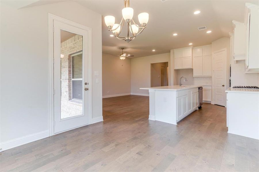 Kitchen featuring white cabinetry, light hardwood / wood-style flooring, backsplash, ceiling fan with notable chandelier, and an island with sink