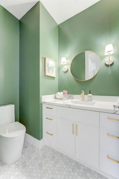 This gorgeous green half bathroom has custom pendant lighting, gold hardware, white cabinetry, quartz countertops, and chic patterned tile flooring.