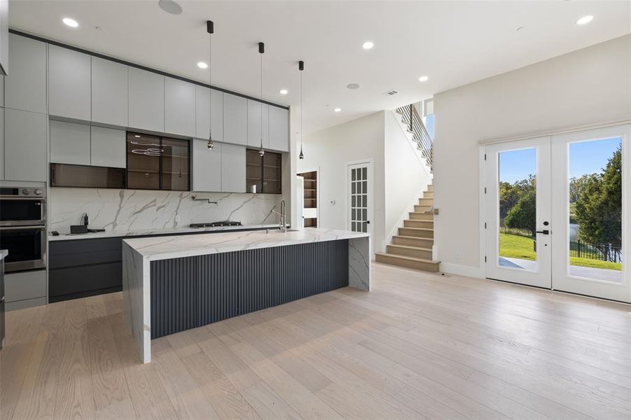 Kitchen featuring a large island with sink, light wood-type flooring, light stone countertops, french doors, and pendant lighting