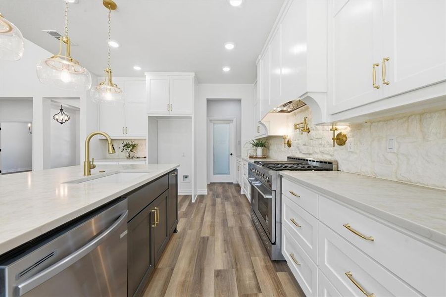 Dual tone kitchen with stainless steel appliances, decorative light fixtures, light wood finished floors, decorative backsplash, and light stone countertops
