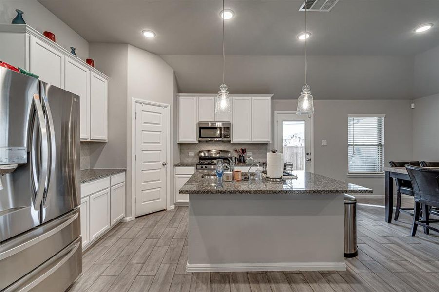 Kitchen with appliances with stainless steel finishes, light hardwood / wood-style flooring, decorative light fixtures, and white cabinets