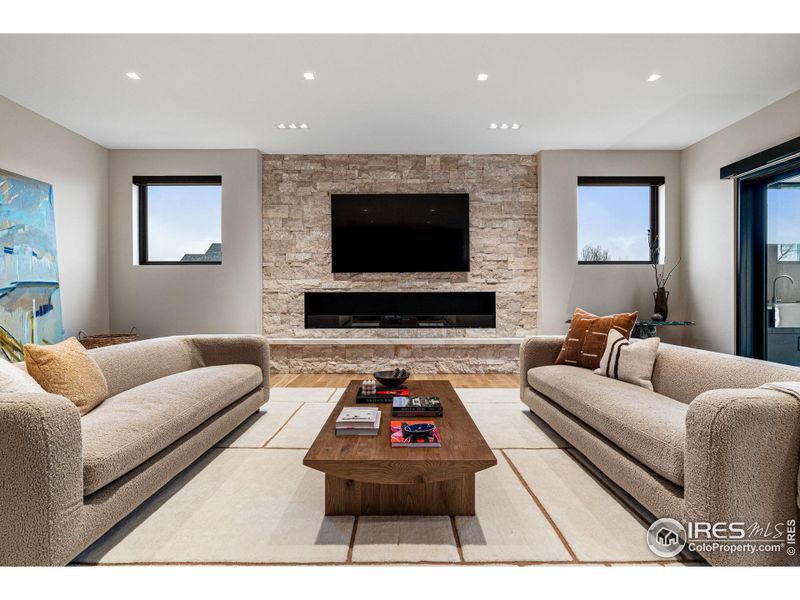 Cinematic bliss in the cozy family room, where every scene comes to life with 5.1 surround sound, an 85" Samsung 4K TV, in ceiling speakers & in wall subwoofer. EcoSmart Flex Series fireplace with textured stone and Pental Quartz slab bench top.