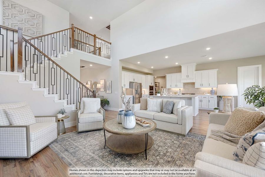 Open-concept living room with two-story staircase, hardwood floors, and white kitchen visible in background.