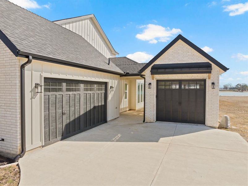 View of front facade featuring a garage, brick siding, driveway, and board and batten siding View of front facade featuring a garage, brick siding, driveway, and board and batten siding