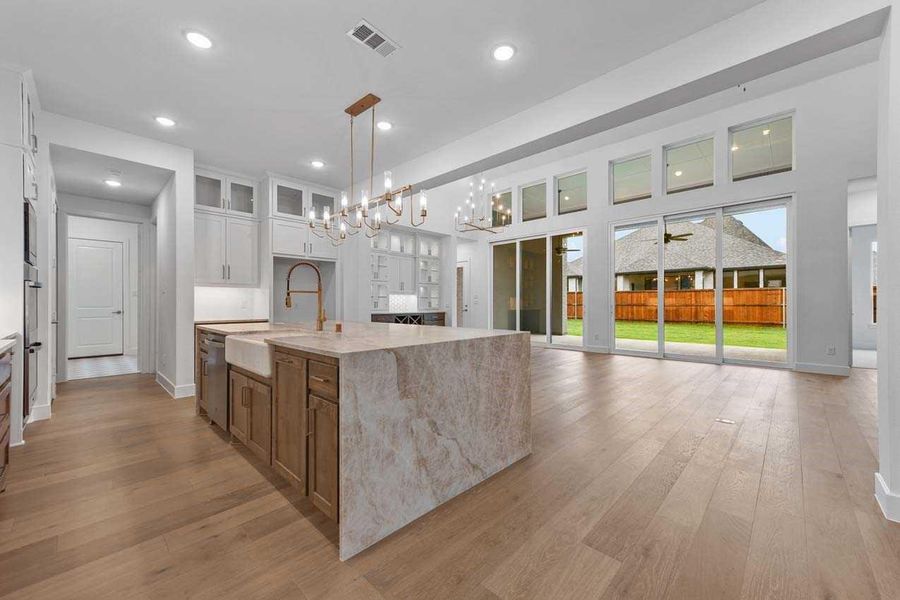 Kitchen with hanging light fixtures, sink, white cabinets, light stone counters, and a kitchen island with sink