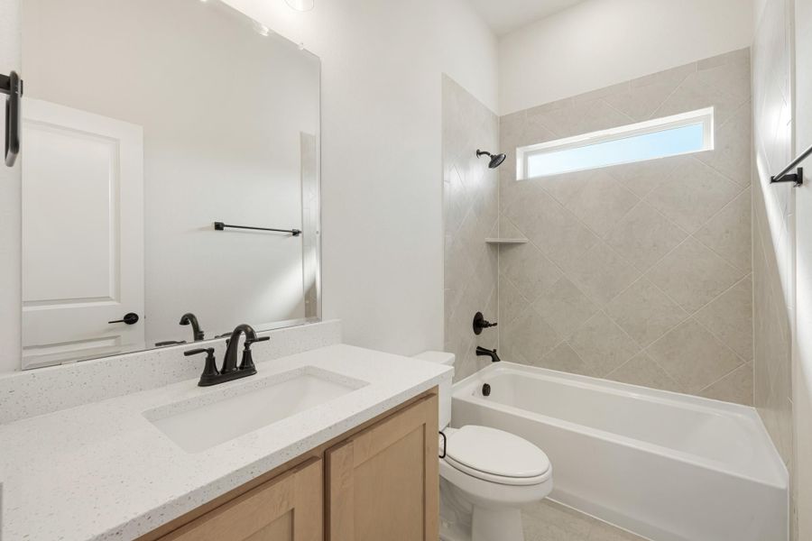 Bathroom with quartz vanity, wood cabinets, tub-shower combo with diagonal tile, and black fixtures