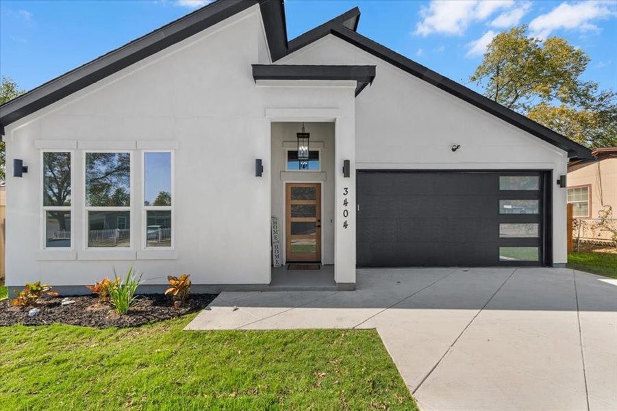 Contemporary home featuring an attached garage, stucco siding, driveway, and a front lawn