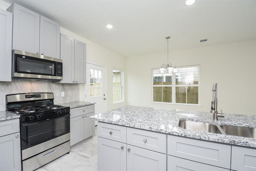 Modern kitchen with white cabinetry, stainless steel appliances, granite countertops, and a window overlooking a fenced backyard.