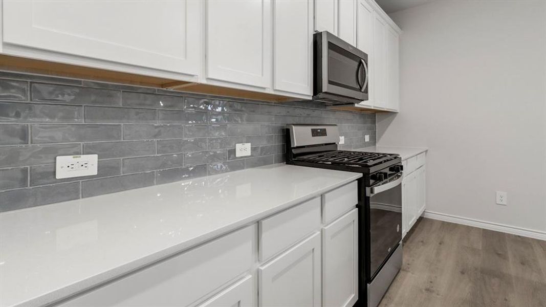 Kitchen featuring stainless steel appliances, white cabinets, tasteful backsplash, light wood-style flooring, and light stone counters