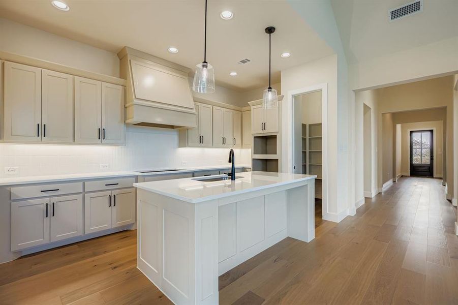 Kitchen featuring decorative light fixtures, decorative backsplash, light stone countertops, an island with sink, and light wood-style floors Kitchen featuring decorative light fixtures, decorative backsplash, light stone countertops, an island with sink, and light wood-style floors