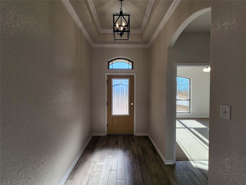 Doorway to outside featuring a textured wall, arched walkways, wood finished floors, a raised ceiling, and crown molding
