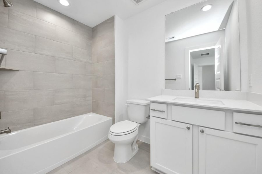 Secondary bath features tile flooring, bath/shower combo with tile surround, light stained wood cabinets, beautiful light countertop.