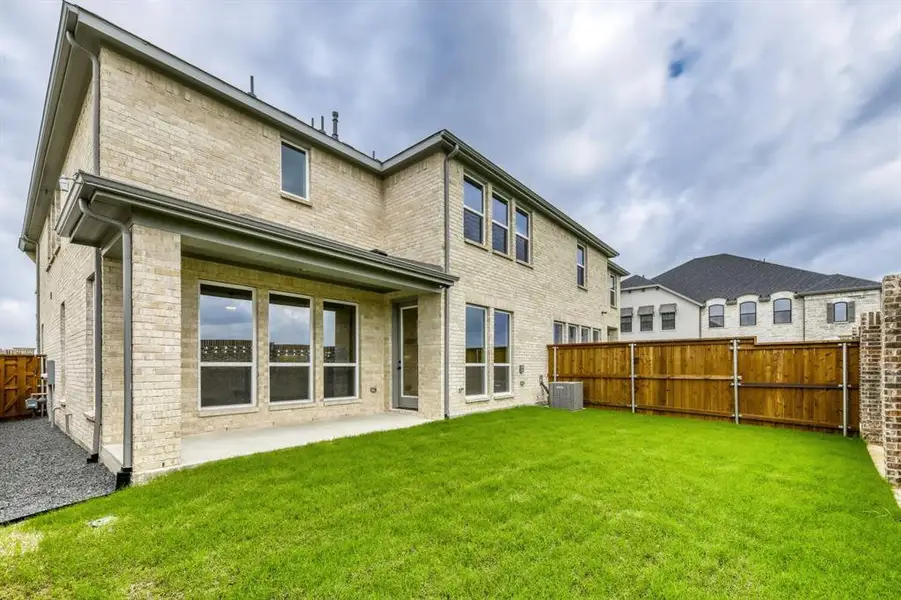 Expansive green lawn with a covered patio, brick exterior, and a wood fence
